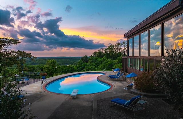 pool at dusk with a patio area and a diving board