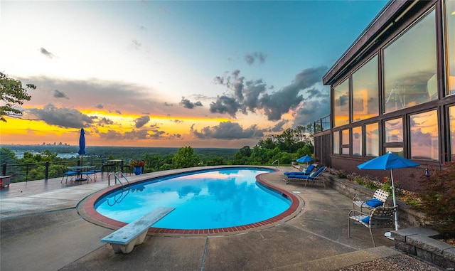 pool at dusk with a patio area and a diving board