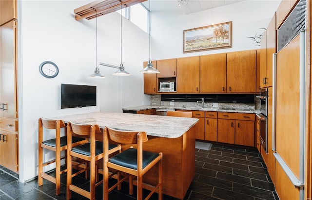 kitchen with a towering ceiling, appliances with stainless steel finishes, tasteful backsplash, brown cabinetry, and a kitchen bar