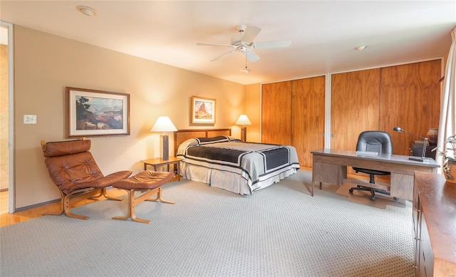 bedroom with ceiling fan, wooden walls, multiple closets, and light carpet