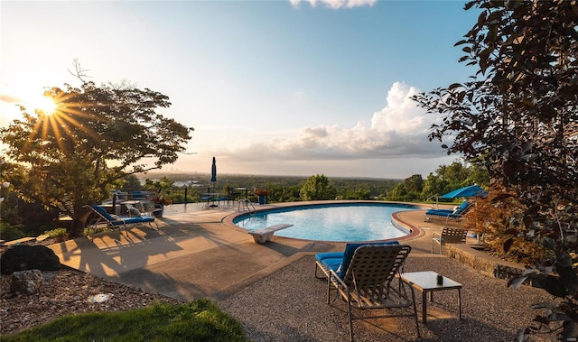 pool at dusk featuring a diving board and a patio area