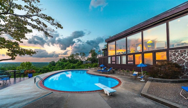 pool at dusk with a patio area and a diving board