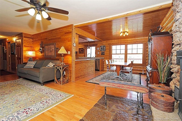 living area with a ceiling fan, light wood-type flooring, wood ceiling, and wooden walls