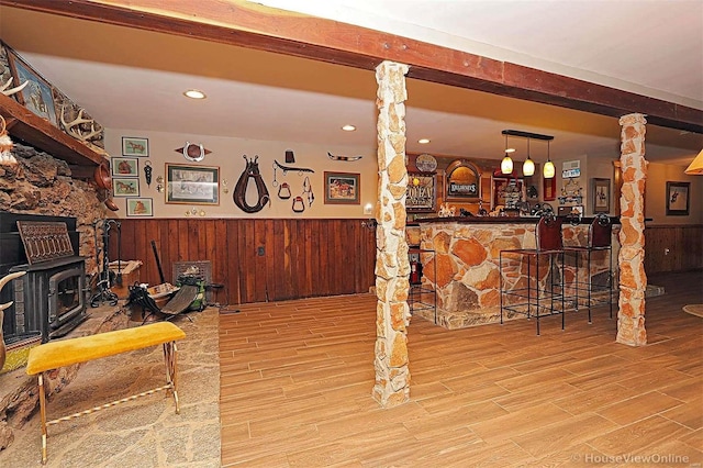 bar with a wood stove, a bar, wood finished floors, and wainscoting