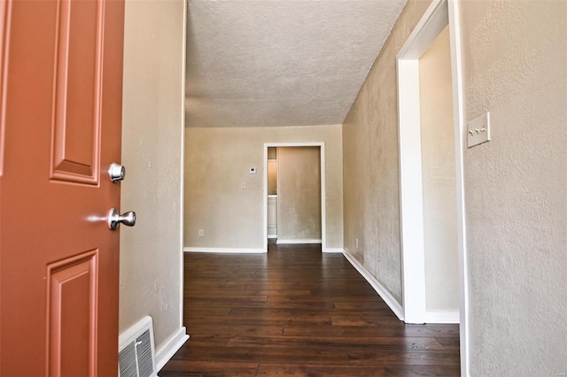 hall with a textured ceiling and dark wood-type flooring