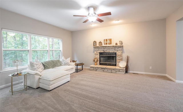 carpeted living area with ceiling fan, a stone fireplace, and baseboards