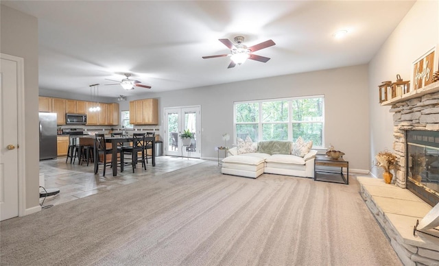 living room featuring light carpet, a fireplace, a ceiling fan, and baseboards