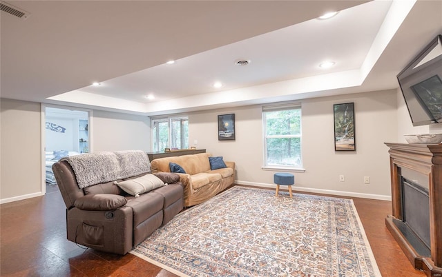 living room featuring a tray ceiling, a fireplace, visible vents, and baseboards