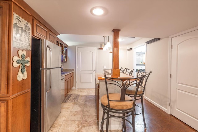 kitchen with baseboards, light countertops, freestanding refrigerator, brown cabinets, and stone finish floor