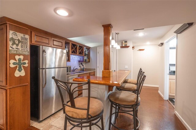 kitchen with a sink, baseboards, freestanding refrigerator, brown cabinetry, and a kitchen bar