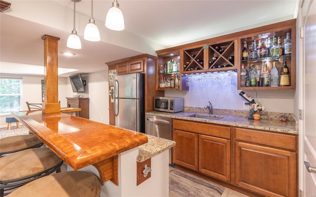 kitchen featuring a breakfast bar area, brown cabinets, light stone countertops, stainless steel appliances, and a sink