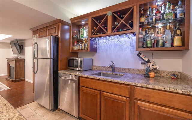 kitchen with appliances with stainless steel finishes, brown cabinets, a sink, and light stone counters