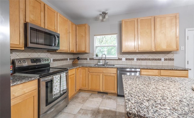 kitchen with appliances with stainless steel finishes, stone countertops, a sink, and decorative backsplash