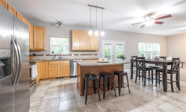 kitchen featuring stainless steel appliances, a kitchen island, backsplash, and light brown cabinetry