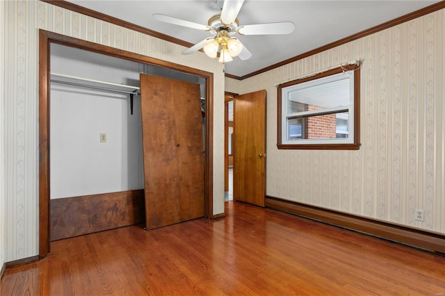 unfurnished bedroom featuring a closet, wood-type flooring, ornamental molding, a baseboard heating unit, and ceiling fan