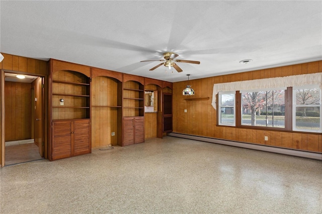 unfurnished living room with wood walls, a textured ceiling, baseboard heating, and ceiling fan