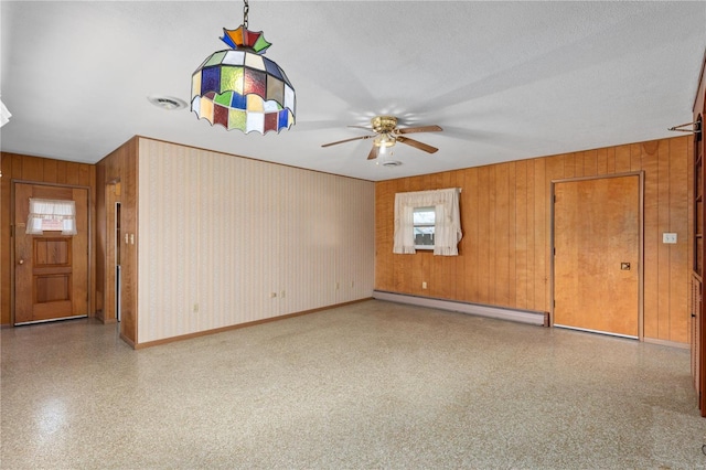 spare room featuring wood walls, a textured ceiling, baseboard heating, and ceiling fan