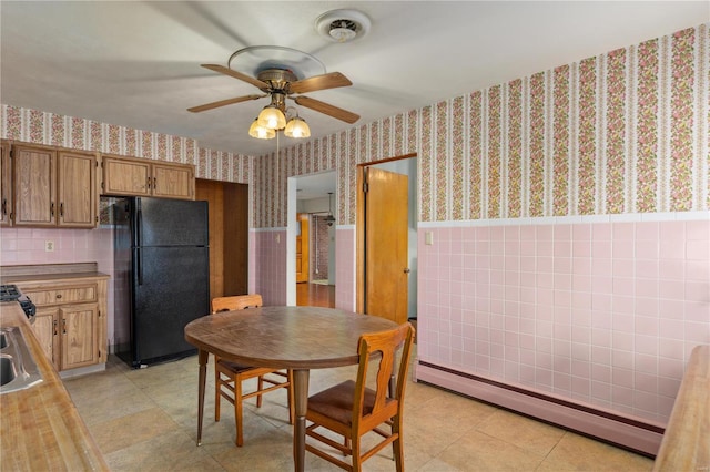 dining room with tile walls, light tile patterned floors, sink, baseboard heating, and ceiling fan