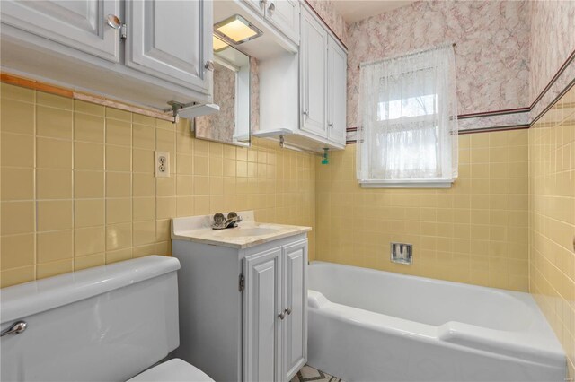 bathroom with tile walls, a washtub, vanity, and toilet