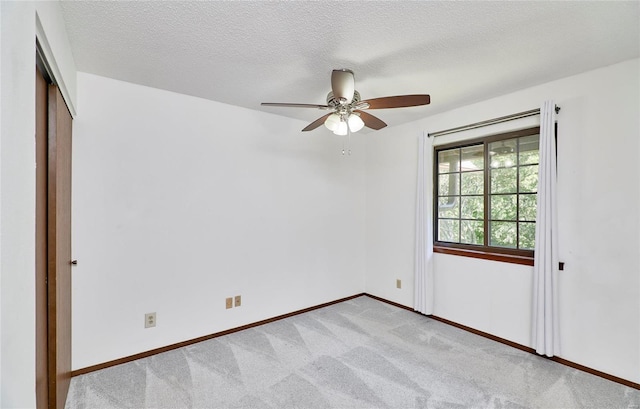 unfurnished room with light carpet, a ceiling fan, baseboards, and a textured ceiling