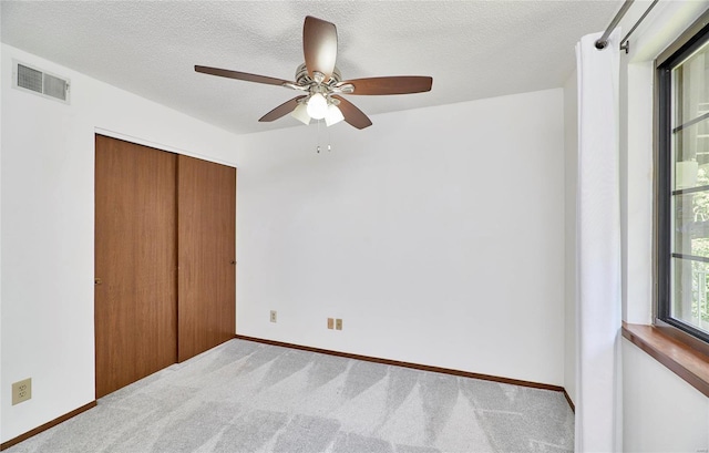 unfurnished bedroom with a textured ceiling, a closet, carpet, and visible vents