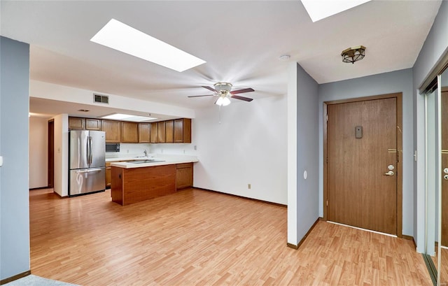 kitchen featuring light wood-style flooring, a peninsula, visible vents, light countertops, and freestanding refrigerator