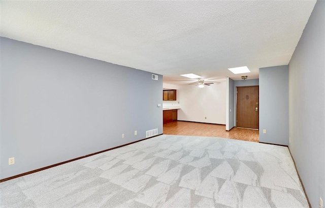 unfurnished room featuring ceiling fan, a textured ceiling, a skylight, and visible vents