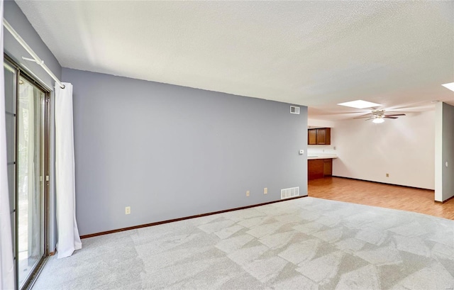 spare room with light carpet, a skylight, visible vents, and a textured ceiling