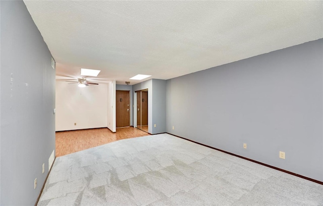 carpeted empty room with a skylight, a ceiling fan, baseboards, and a textured ceiling