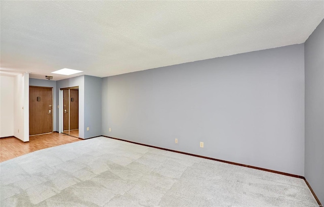 unfurnished room featuring light carpet, a textured ceiling, a skylight, and baseboards