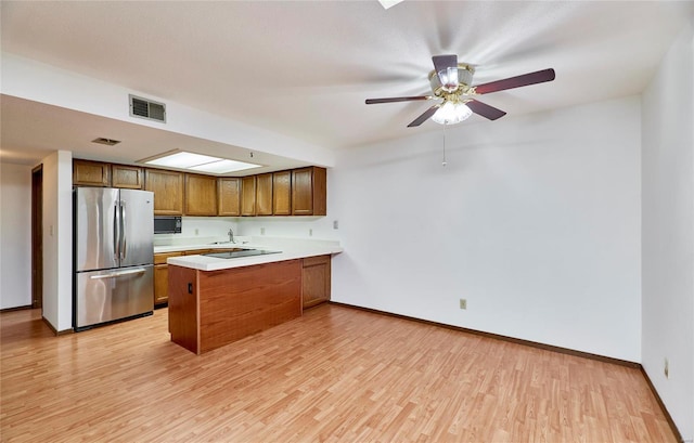 kitchen featuring black microwave, a peninsula, visible vents, light countertops, and freestanding refrigerator