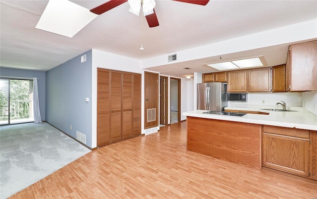 kitchen with a skylight, visible vents, brown cabinets, black appliances, and a sink