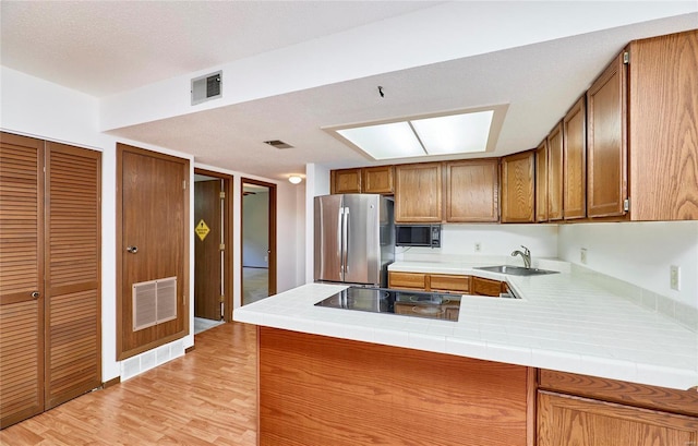 kitchen featuring black appliances, brown cabinetry, a sink, and visible vents