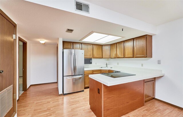 kitchen featuring a peninsula, black appliances, visible vents, and brown cabinetry