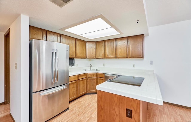 kitchen featuring visible vents, brown cabinetry, stainless steel appliances, light wood-style floors, and a sink