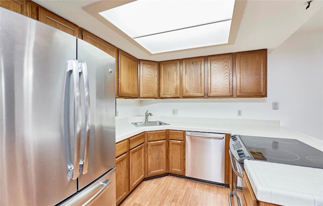 kitchen with appliances with stainless steel finishes, brown cabinetry, a sink, and light wood-style flooring