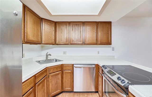 kitchen featuring appliances with stainless steel finishes, light wood-style floors, brown cabinetry, and a sink