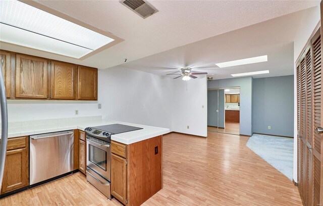 kitchen with ceiling fan, stainless steel appliances, a peninsula, a skylight, and visible vents