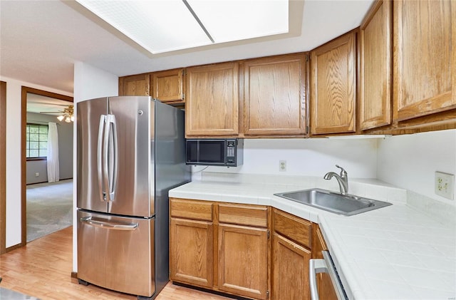 kitchen with tile counters, brown cabinetry, freestanding refrigerator, a sink, and black microwave