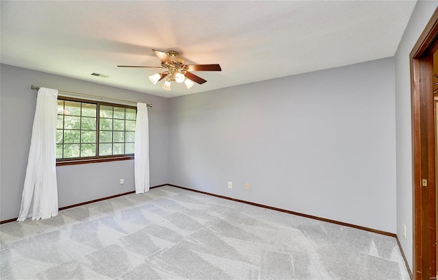 empty room featuring baseboards, visible vents, a ceiling fan, light colored carpet, and a textured ceiling