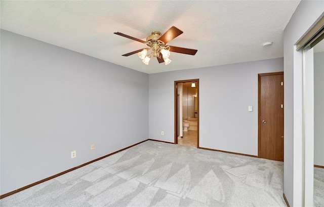 unfurnished bedroom featuring ceiling fan, a textured ceiling, light carpet, baseboards, and ensuite bath