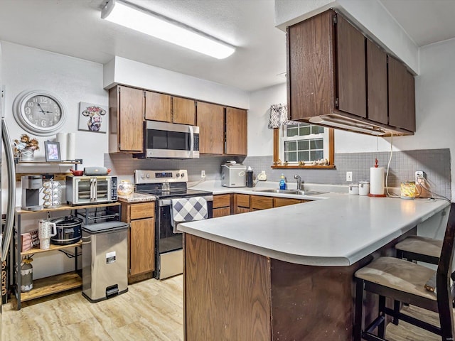 kitchen with appliances with stainless steel finishes, decorative backsplash, kitchen peninsula, light wood-type flooring, and sink