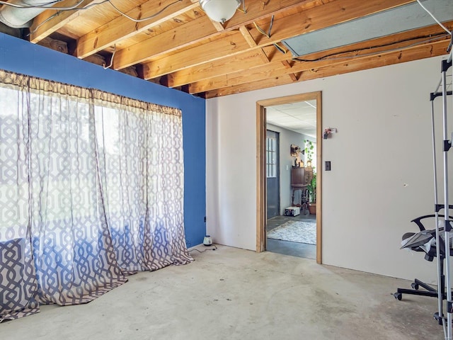 spare room with beam ceiling, a wealth of natural light, and concrete flooring