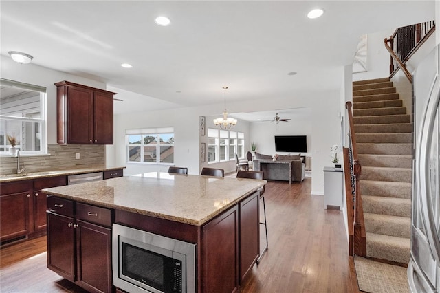 kitchen with a center island, sink, stainless steel appliances, hardwood / wood-style floors, and decorative light fixtures