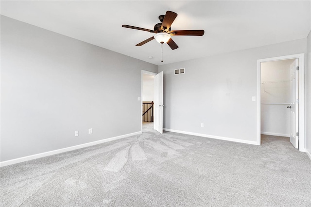 unfurnished bedroom with a walk in closet, ceiling fan, a closet, and light carpet