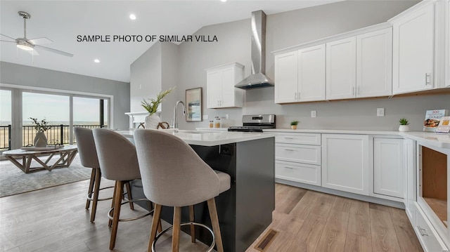 kitchen featuring stainless steel electric range oven, white cabinetry, a center island, light wood-type flooring, and wall chimney exhaust hood