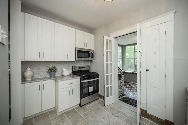 kitchen with appliances with stainless steel finishes, white cabinets, light tile patterned flooring, tasteful backsplash, and light stone counters