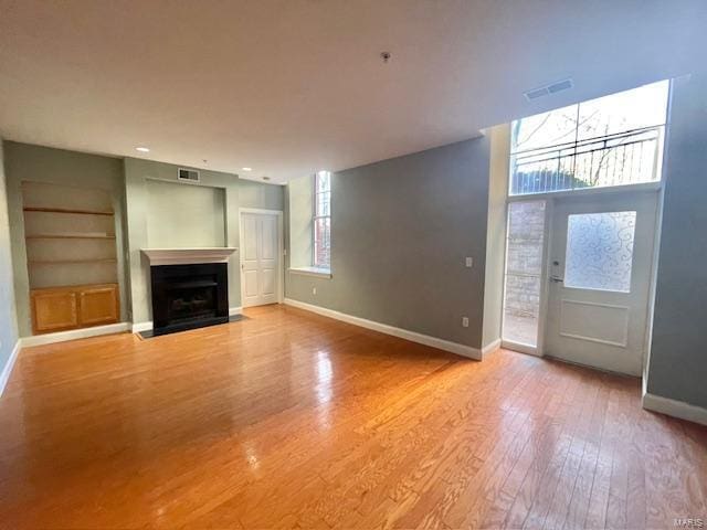 unfurnished living room with hardwood / wood-style flooring, plenty of natural light, and built in shelves