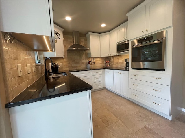 kitchen with tasteful backsplash, appliances with stainless steel finishes, dark stone counters, sink, and wall chimney range hood