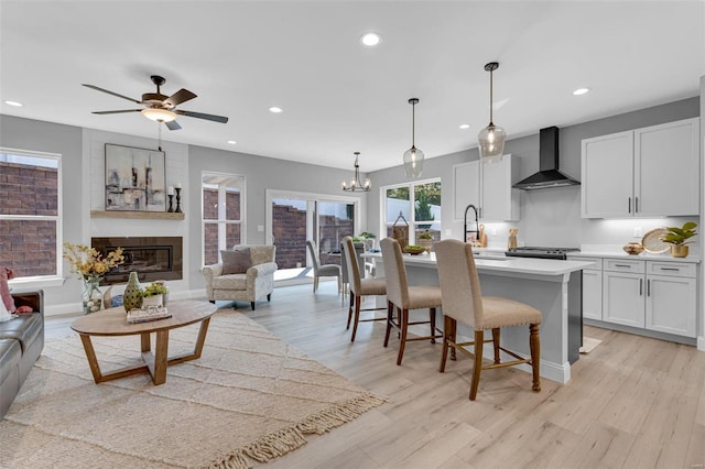 kitchen featuring white cabinetry, a kitchen island with sink, light hardwood / wood-style flooring, pendant lighting, and wall chimney exhaust hood